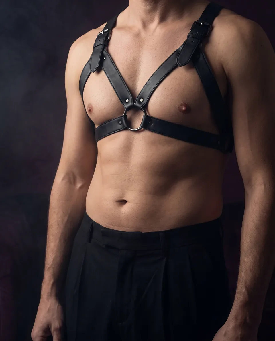 Adult man wearing a black leather chest harness with an O ring, face out of frame